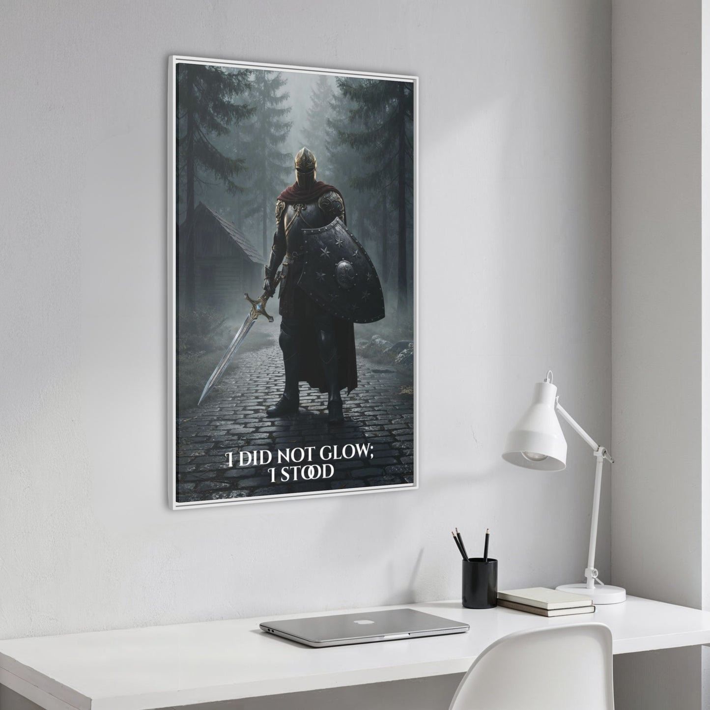 Angled framed ‘I did not glow; I stood’ knight canvas hanging above a clean white workspace with laptop and lamp.