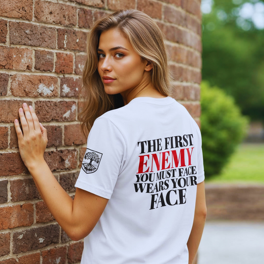 Back view, white organic cotton t-shirt (Stanley/Stella STTU169) with “The first enemy you must face wears your face” quote, ENEMY in red, brick wall, sleeve crest visible.