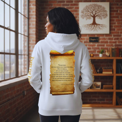 Back view of Amara Solis in the white “Carry the Flame” hoodie, standing by tall loft windows and bookshelves, spotlight on the aged scroll quote on the back, with the golden sleeve typography wrapping her arms as if she’s literally carrying the flame into Chapter 1.