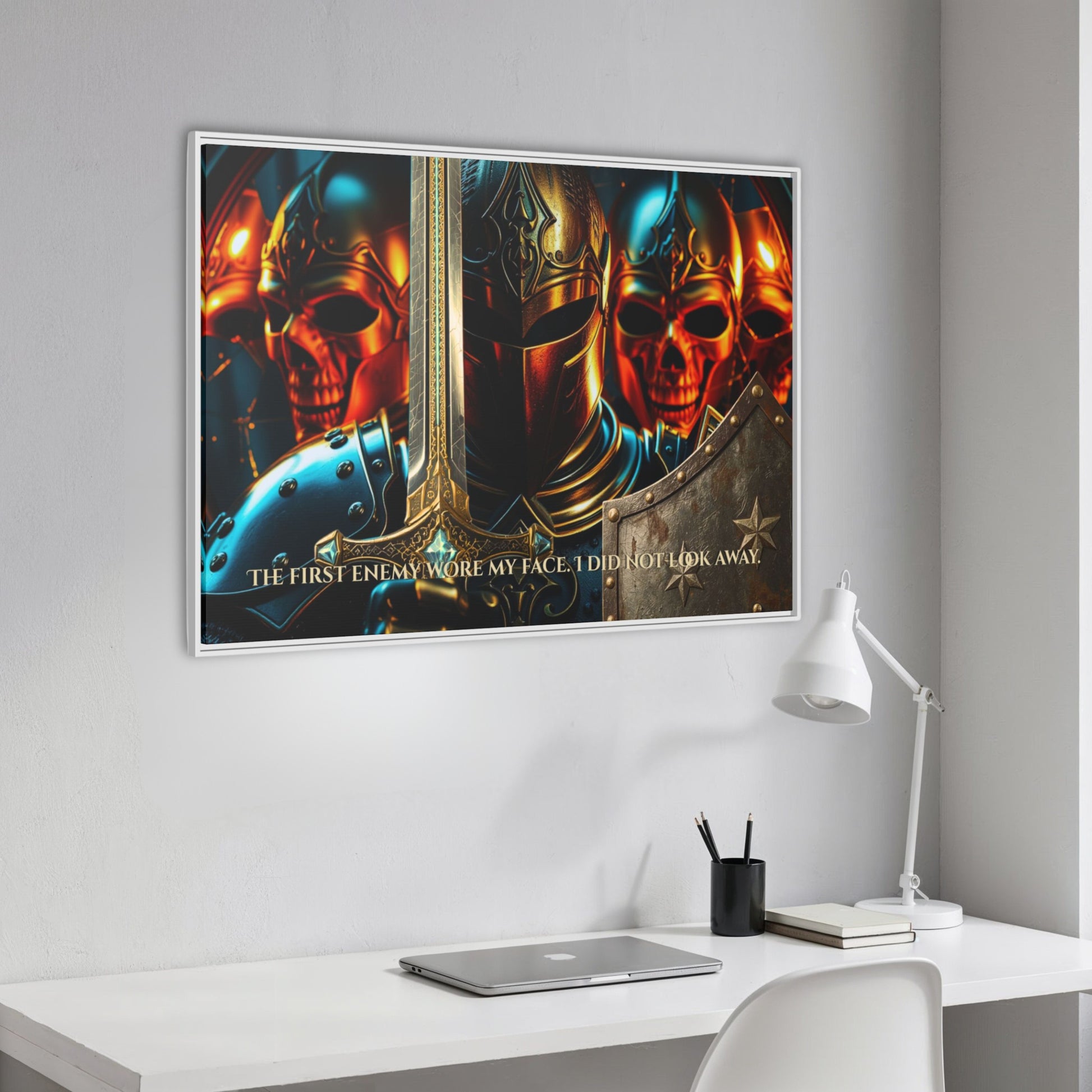 Angled white framed ‘The first enemy wore my face. I did not look away.’ knight and skulls canvas hanging above a clean white workspace with laptop and lamp.