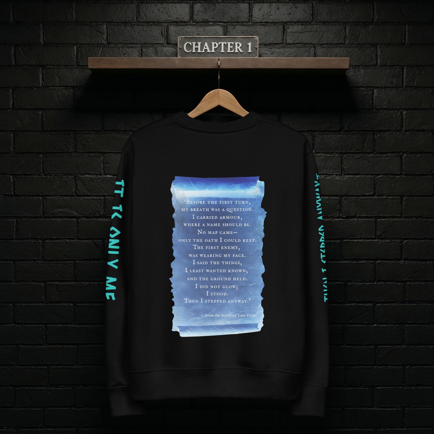Chapter 1 black sweatshirt hanging on a rail against a dark brick wall, back design featuring the blue scroll from the Scroll of Lost Paths and the line “Then I Stepped Anyway”.