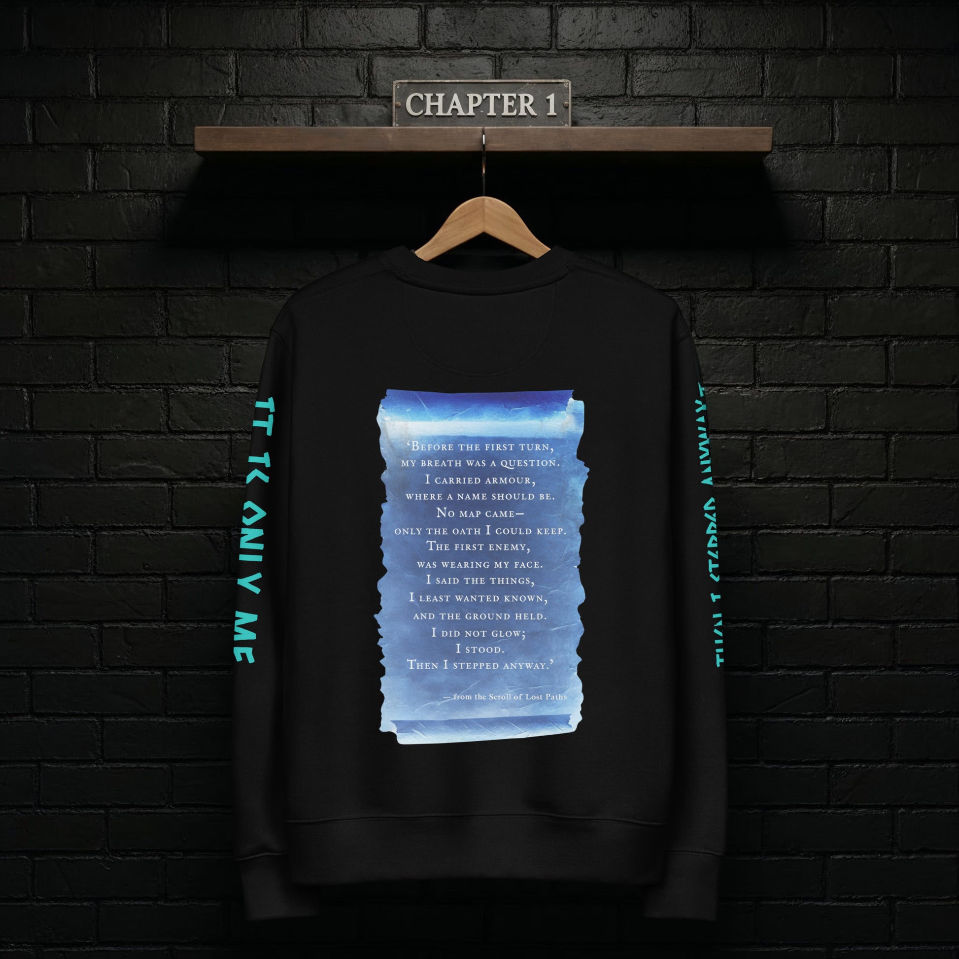 Chapter 1 black sweatshirt hanging on a rail against a dark brick wall, back design featuring the blue scroll from the Scroll of Lost Paths and the line “Then I Stepped Anyway”.