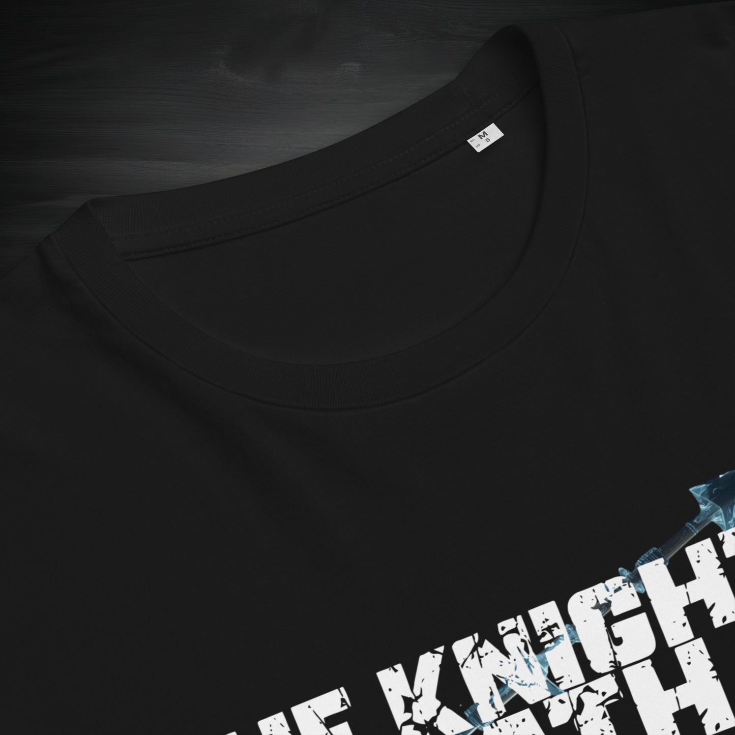 Close-up of the neckline and chest print of a black “The Knight’s Path” organic tee, highlighting stitching, fabric texture, and distressed logo detail.