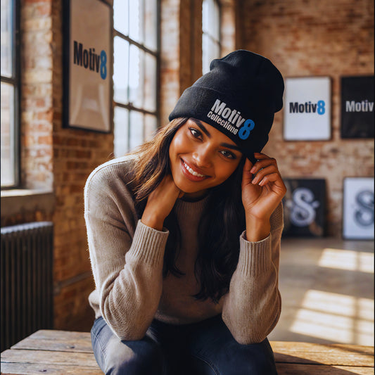 Motiv8 Collections black cuffed beanie with blue 8 logo worn by Amara Solis, smiling and adjusting the hat in the industrial loft, cozy motivational streetwear look.