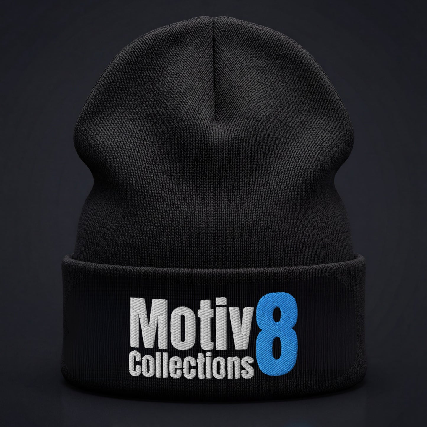 Studio close-up of Motiv8 Collections black cuffed beanie on dark background, blue 8 and white logo embroidery centered and clearly visible.
