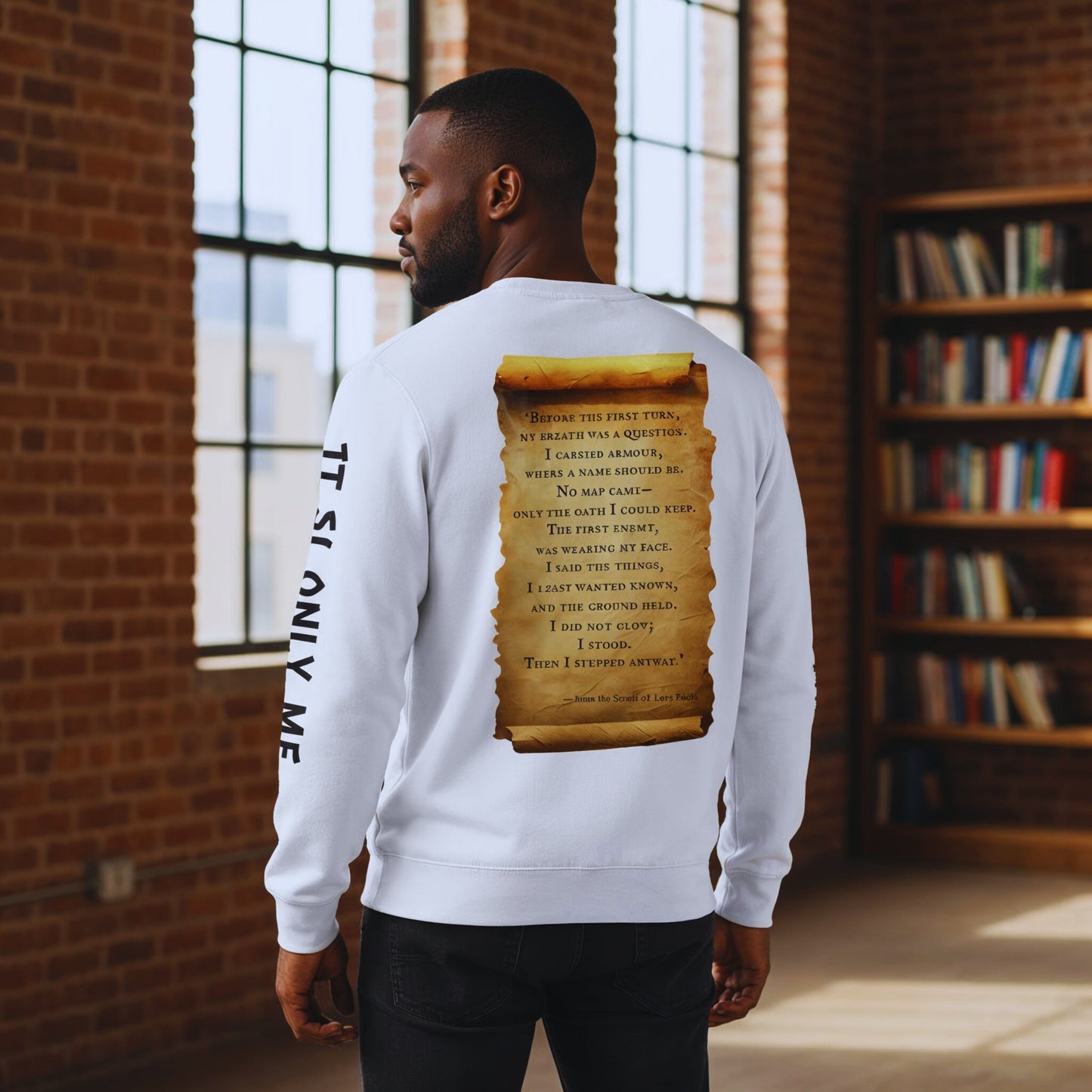 Man in a brick loft library facing away, showing the parchment scroll quote and “IT IS ONLY ME” sleeve text on a white sweatshirt.