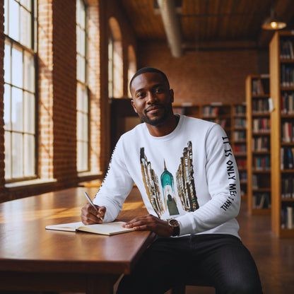 Man writing in a journal at a long wooden table in a loft library while wearing the white book-arch sweatshirt.