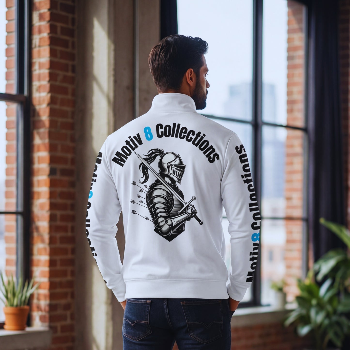 Back view of Adrian in the white Motiv8 Collections track jacket in the Motiv8 loft, focusing on the large knight-with-arrows artwork and curved “Motiv 8 Collections” text across the upper back for a hero graphic shot.