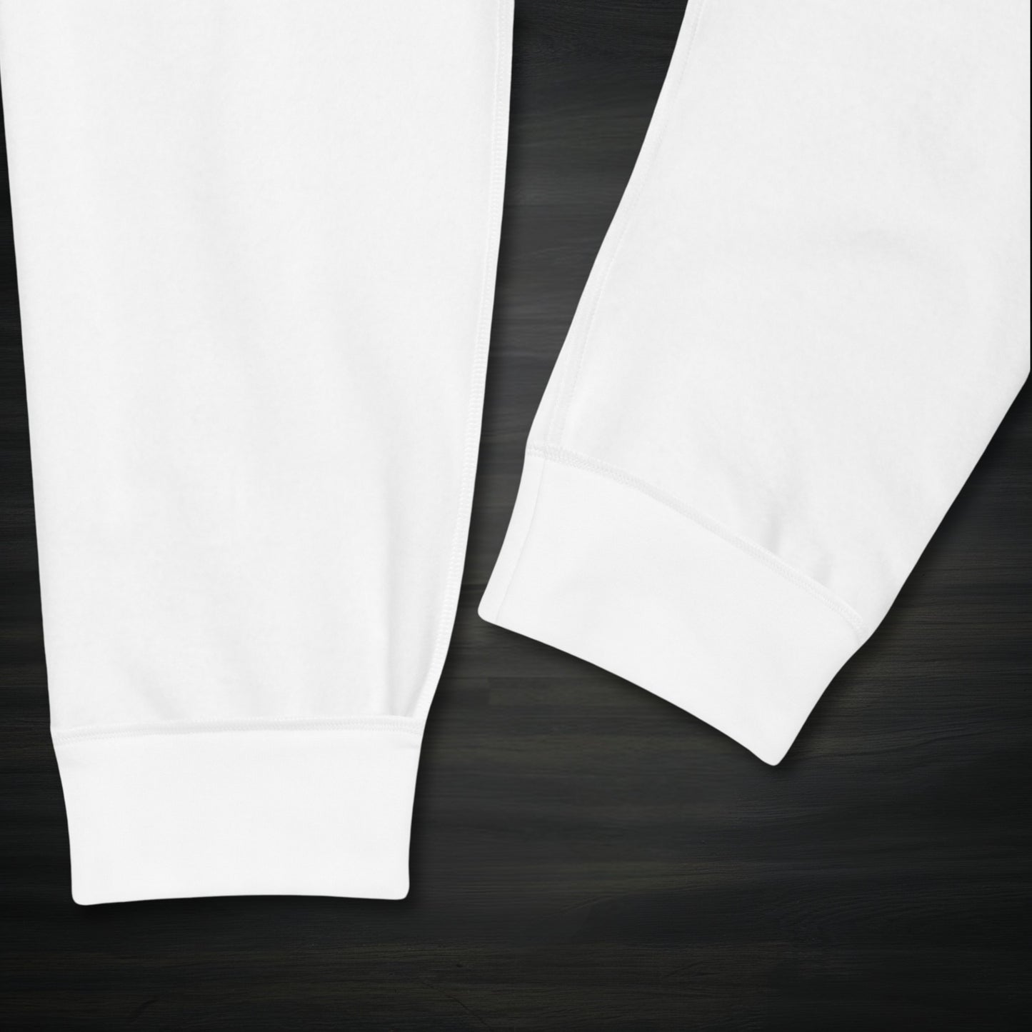 Close-up of the white Motiv8 Collections knight armor joggers ankle cuffs on a dark wooden surface, showing the clean stitching and snug ribbed finish for a secure, stay-put fit.