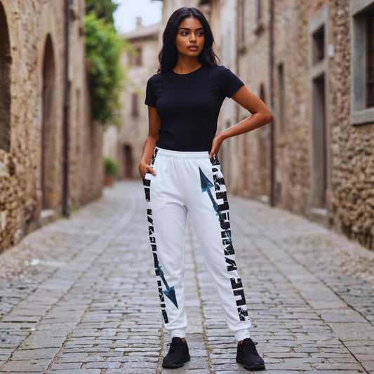 Amara in a black T-shirt and Motiv8 Collections The Knight’s Path “Arrow One” white joggers, standing centred in a cobblestone alley, full arrow print visible on both legs.