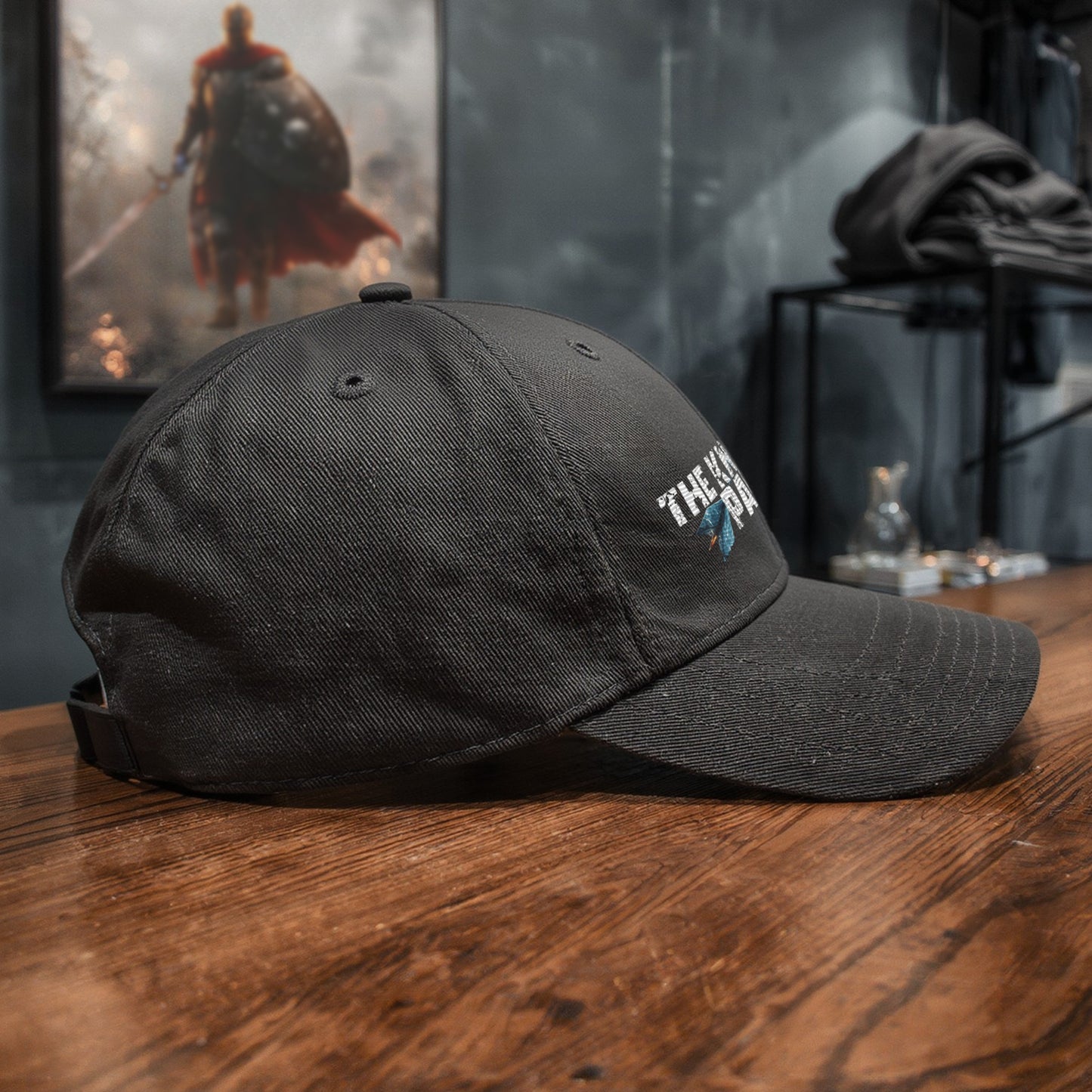 Angled side shot of The Knight’s Path cap in a dim fantasy-inspired store, with warrior artwork blurred in the background to hint at the Knight’s world.