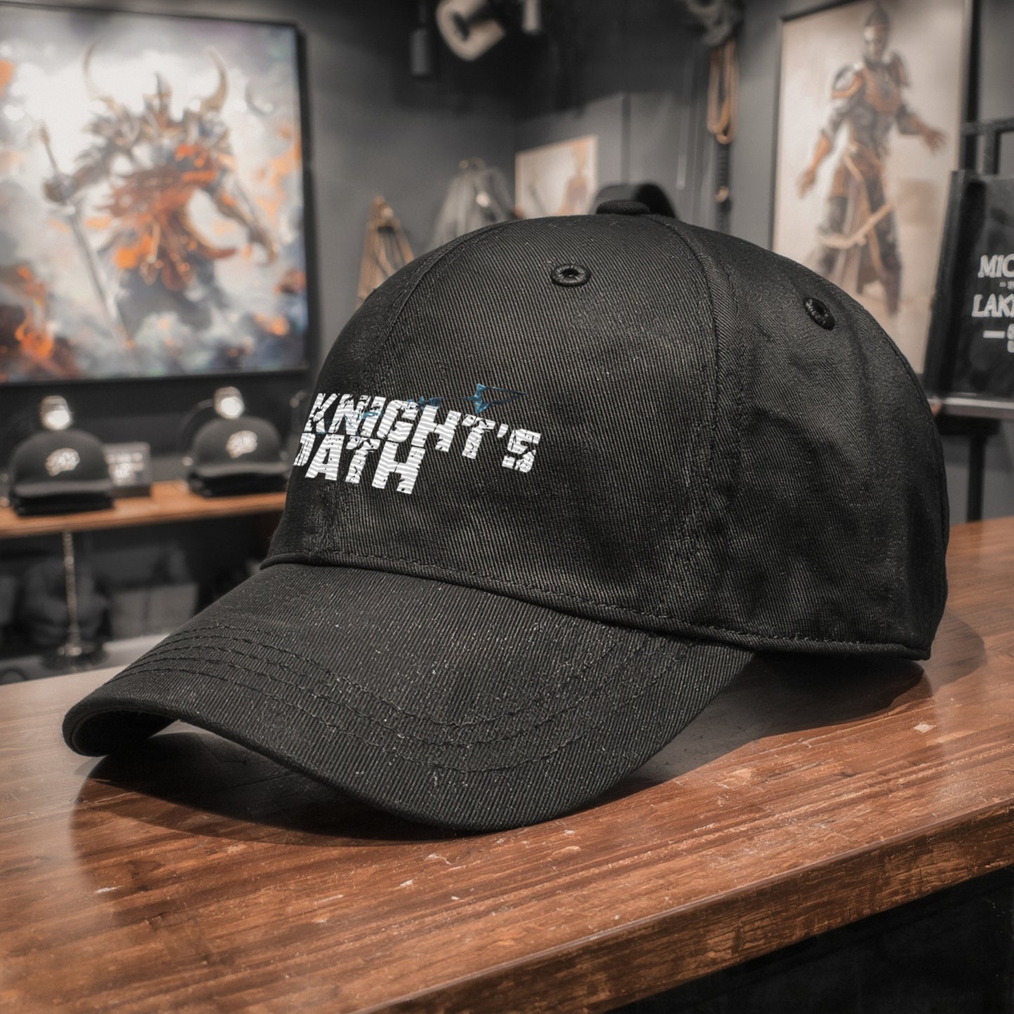 Close-up of The Knight’s Path black cap on a wooden surface, showing the distressed white text and blue crystal arrow embroidery in a modern fantasy retail setting.