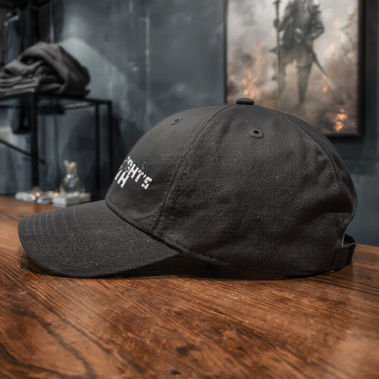 Side view of The Knight’s Path black cap on a wooden counter, curved brim and structured crown visible against a dark fantasy shop interior.