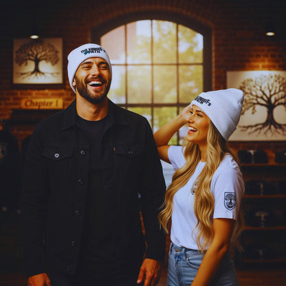 Male and female models wearing white The Knight’s Path beanies, laughing together in front of the large arched window and Chapter 1 tree artwork inside the Motiv8 store.