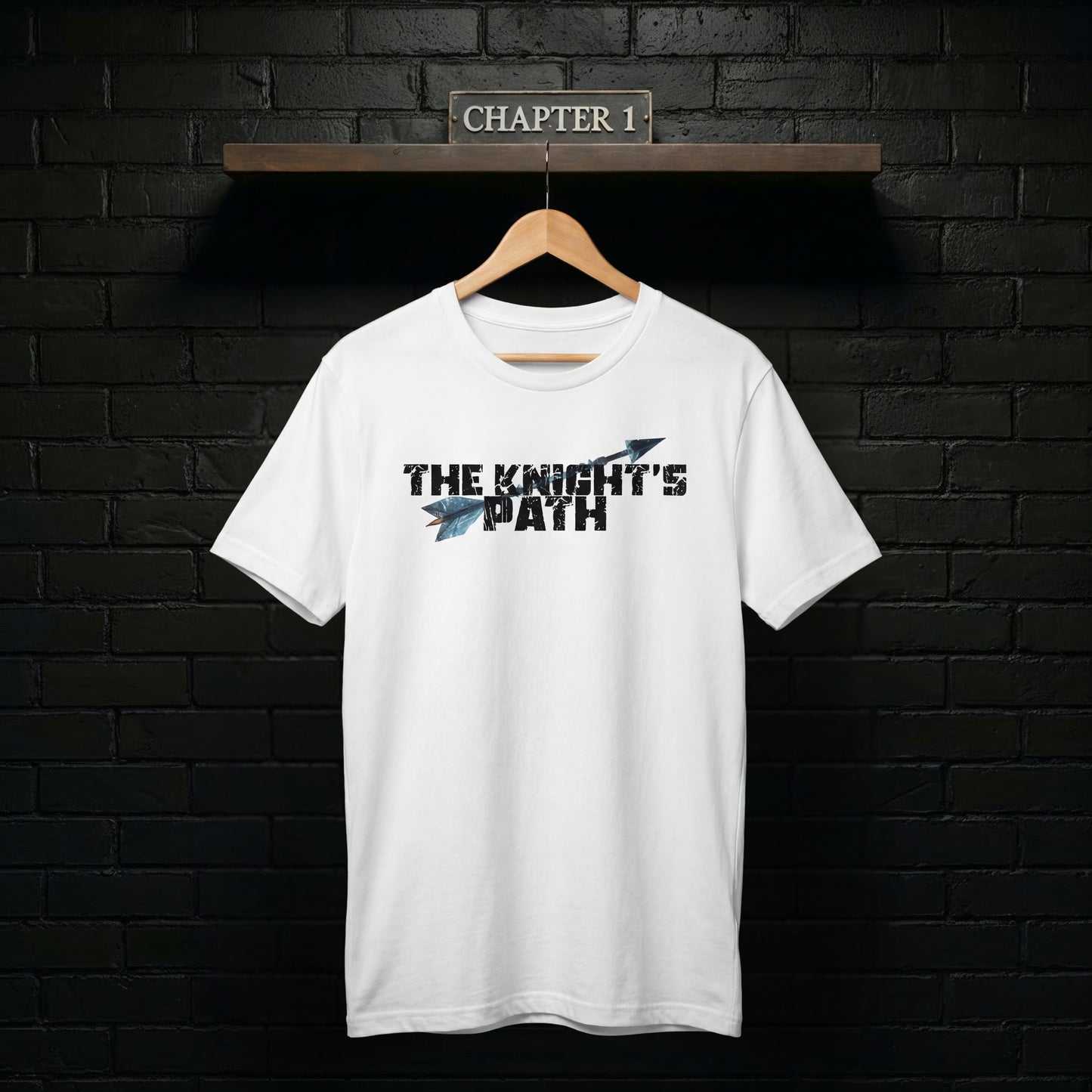 The Knight’s Path Chapter 1 white t-shirt on a wooden hanger against a black brick wall with “Chapter 1” sign, clean product mockup highlighting the arrow logo.